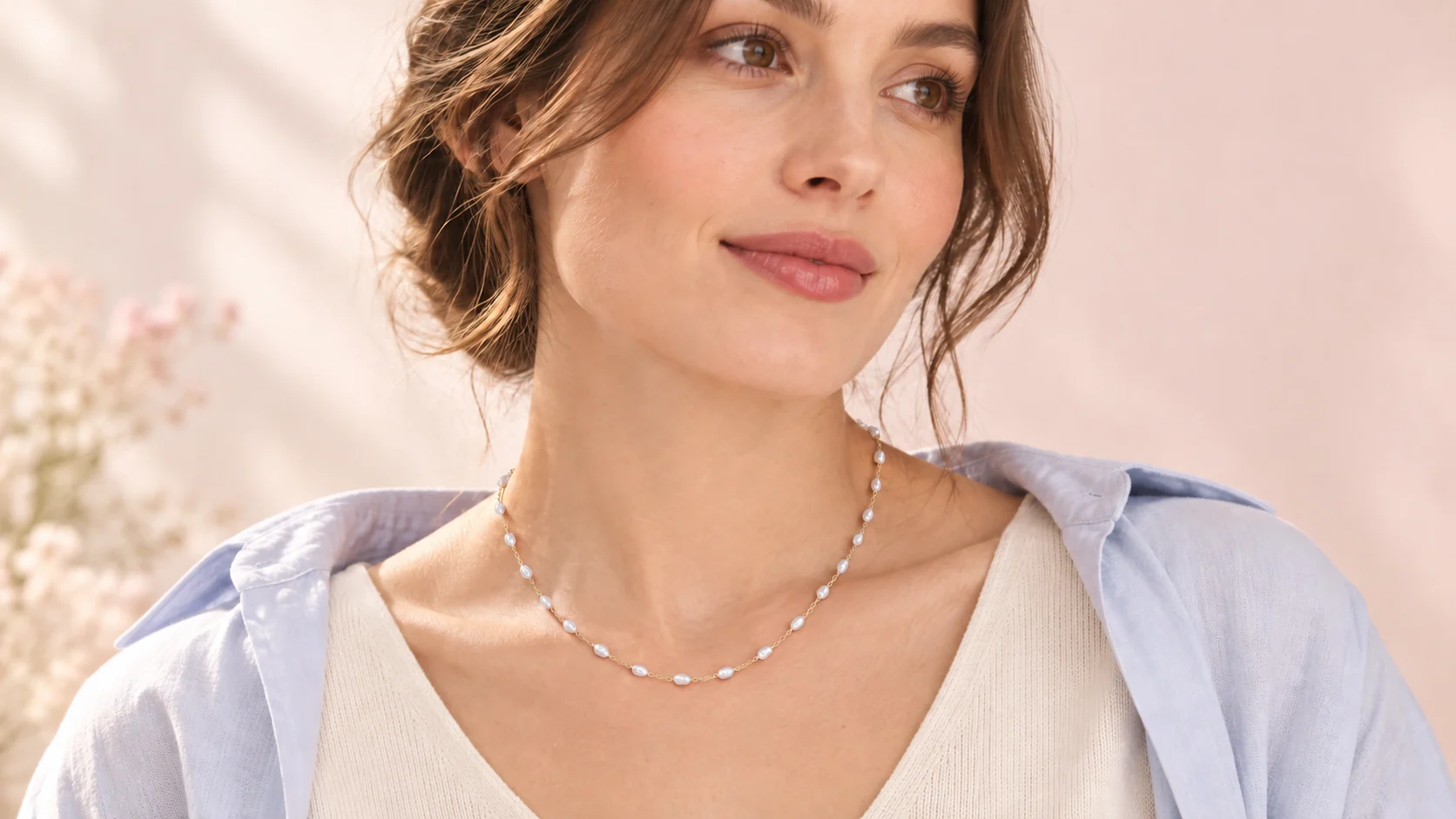 An adult model wearing a necklace with small irregular white pearls and fine links